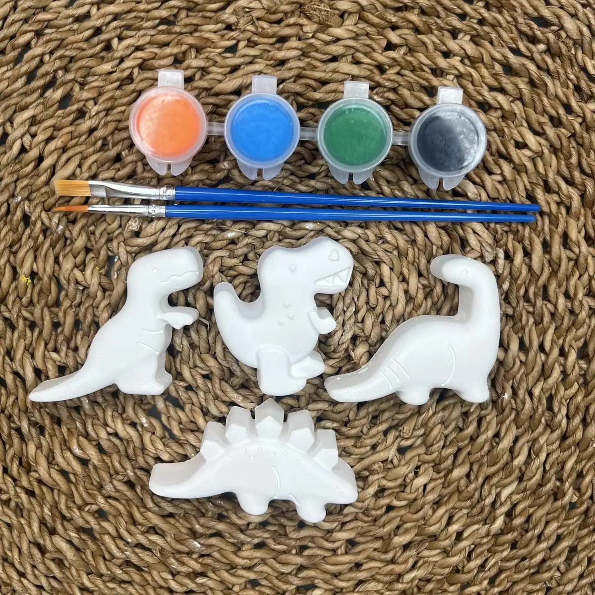 Four white plaster dinosaurs with orange, blue, green, and black paint and two brushes
