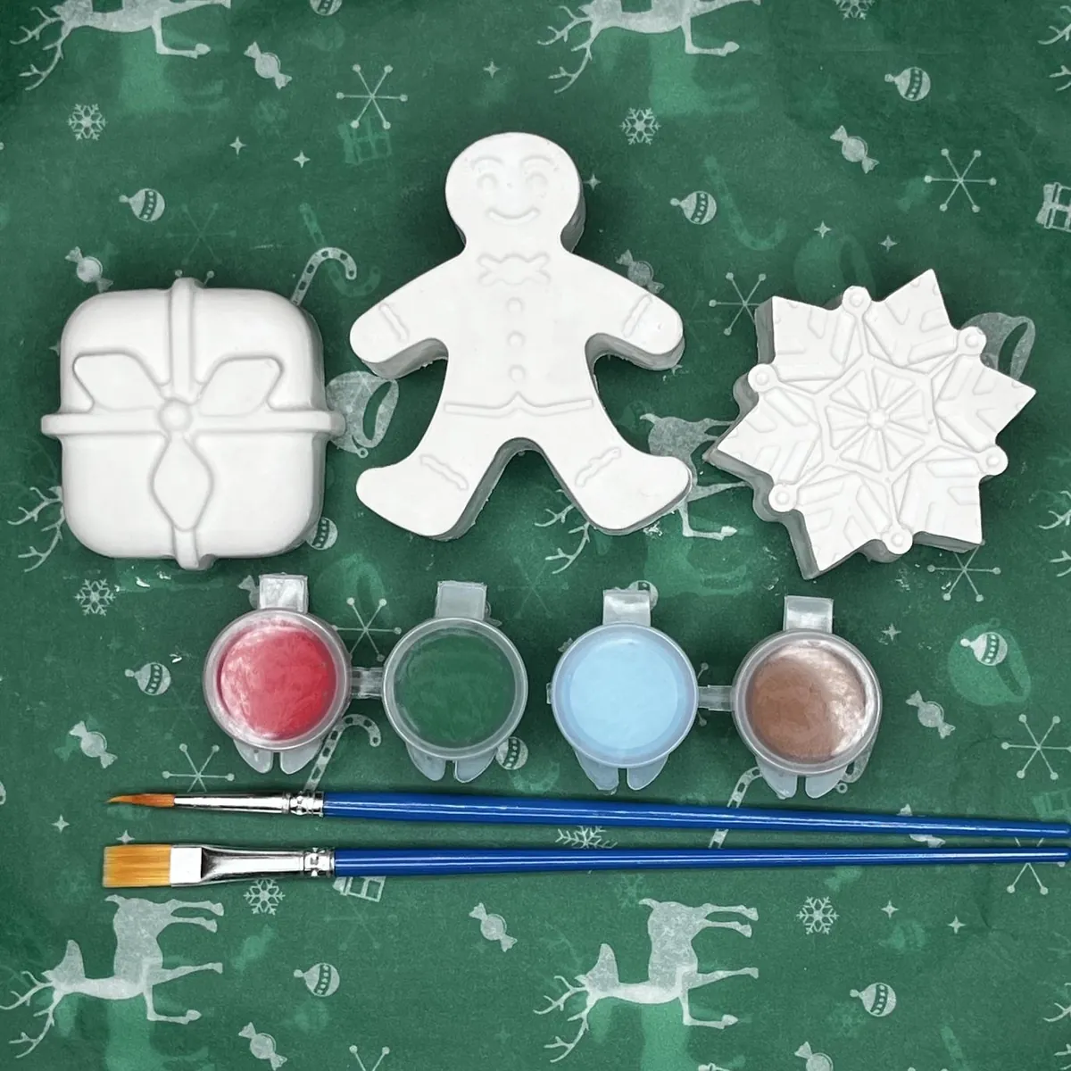 White plaster gift, gingerbread man, and snowflake with red, green, blue, and brown paint and two brushes